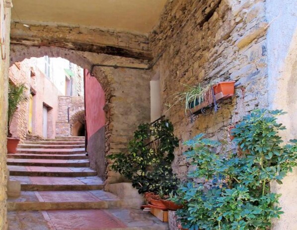 A narrow stone staircase leading to a doorway, flanked by potted plants and a small orange cart.