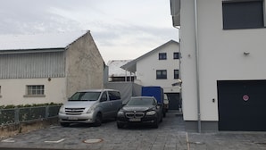 Ein Parkplatz mit zwei Autos, ein Gebäude mit Garage und eine weiße Wand mit einem Verbotsschild.