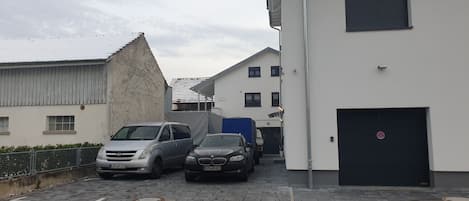 A parking area with two cars, a building with a garage, and a white wall with a no parking sign.