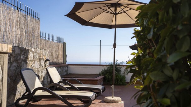 Eine Terrasse mit Liegestühlen und einem großen Sonnenschirm, mit Blick auf ein Gewässer.