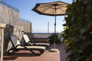 Une terrasse avec des chaises longues et un grand parasol, donnant sur une étendue d’eau.