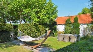 A hammock in a garden with a white building in the background. - Het Zoete Peerd (Groede)