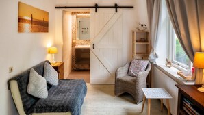 A cozy room with a sofa, a chair, a small table, a lamp, and a window with curtains. - Het Zoete Peerd (Groede)