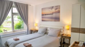 A double room with two beds, a view of greenery outside, a painting on the wall, and bedside lamps. - Het Zoete Peerd (Groede)