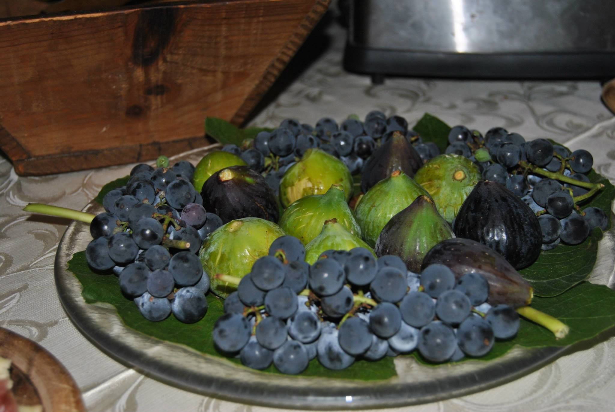 A plate with green figs and grapes on a tablecloth.