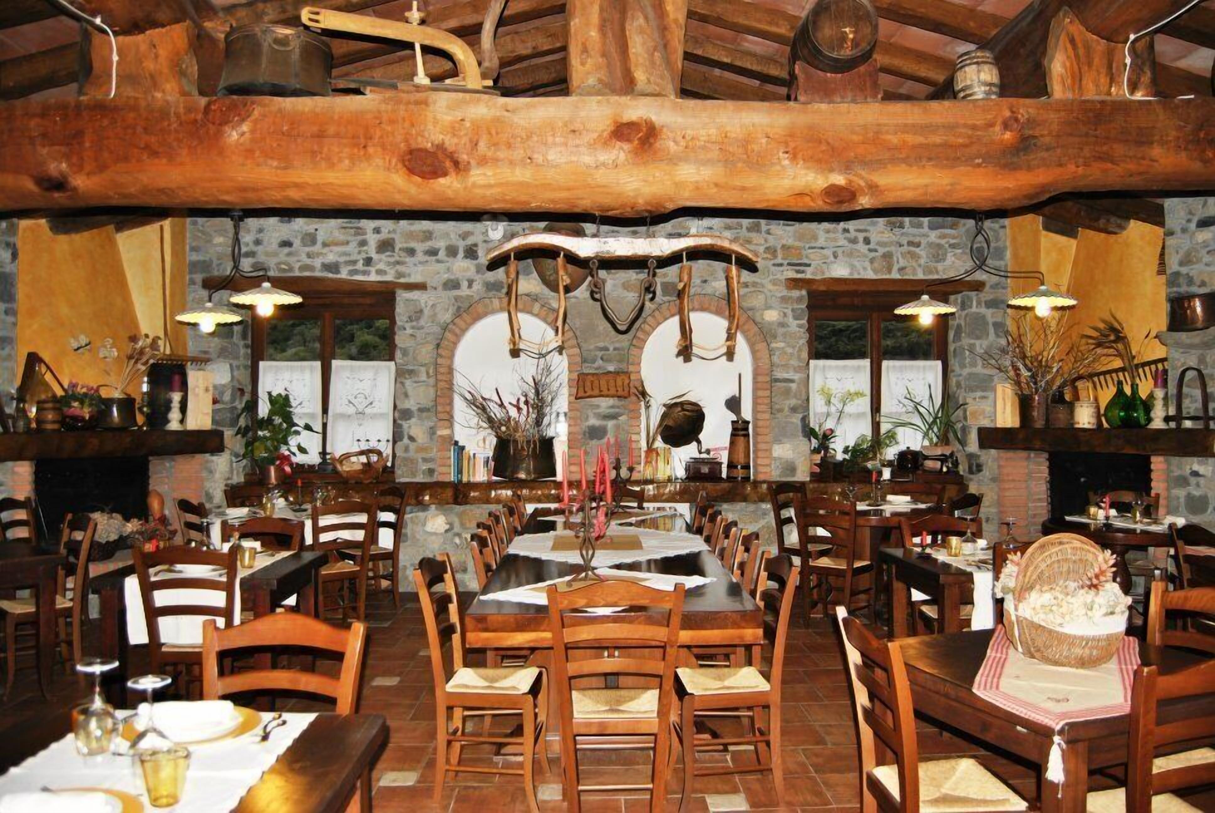 A rustic dining area with wooden tables and chairs, stone walls, and hanging light fixtures.