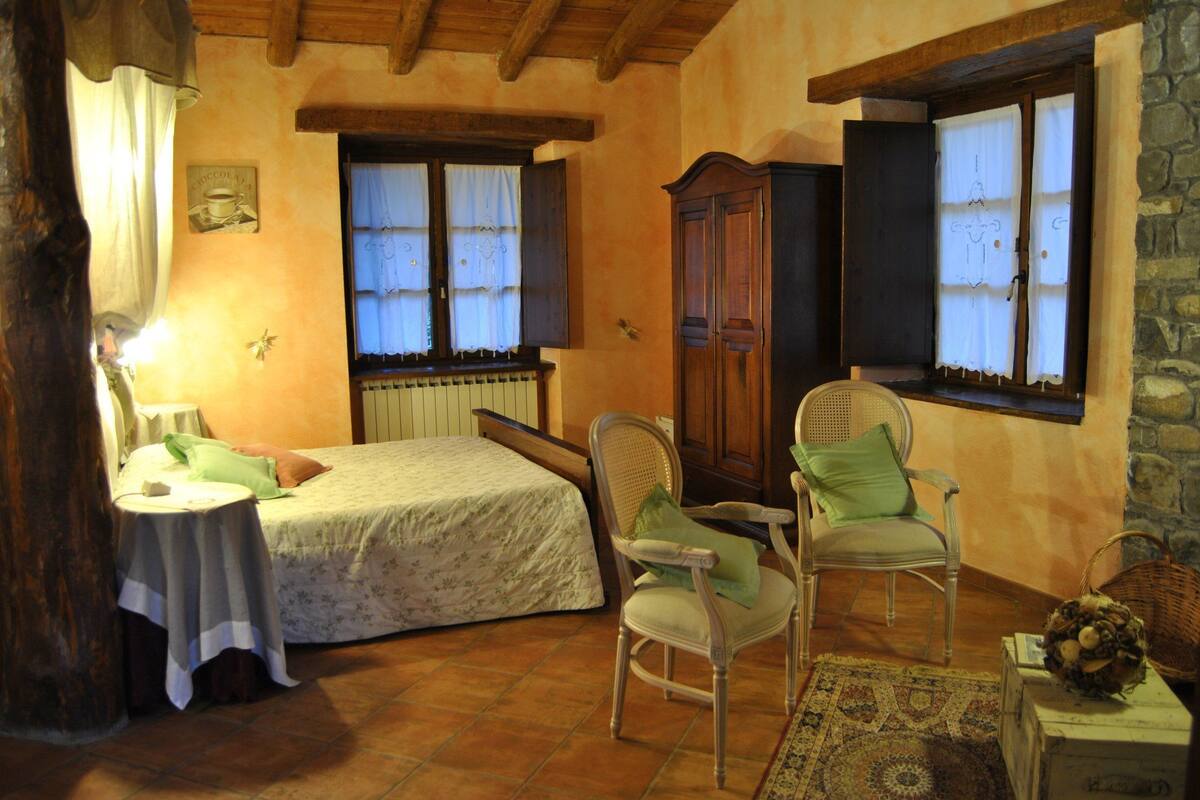 A cozy bedroom with a bed, two chairs, a small table, and a window with curtains.
