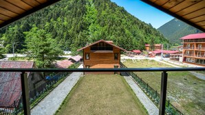 Una cabaña de madera con balcón, rodeada de un paisaje montañoso y otras construcciones.