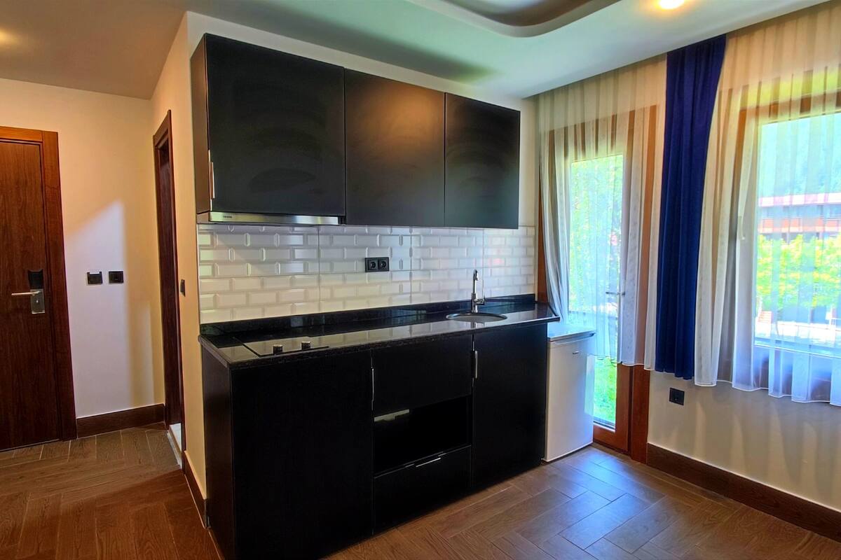A modern kitchen with dark cabinetry, a white tiled backsplash, and a large window with curtains.