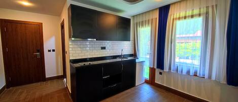Una cocina moderna con armarios oscuros, salpicadero de azulejos blancos y un amplio ventanal con cortinas.