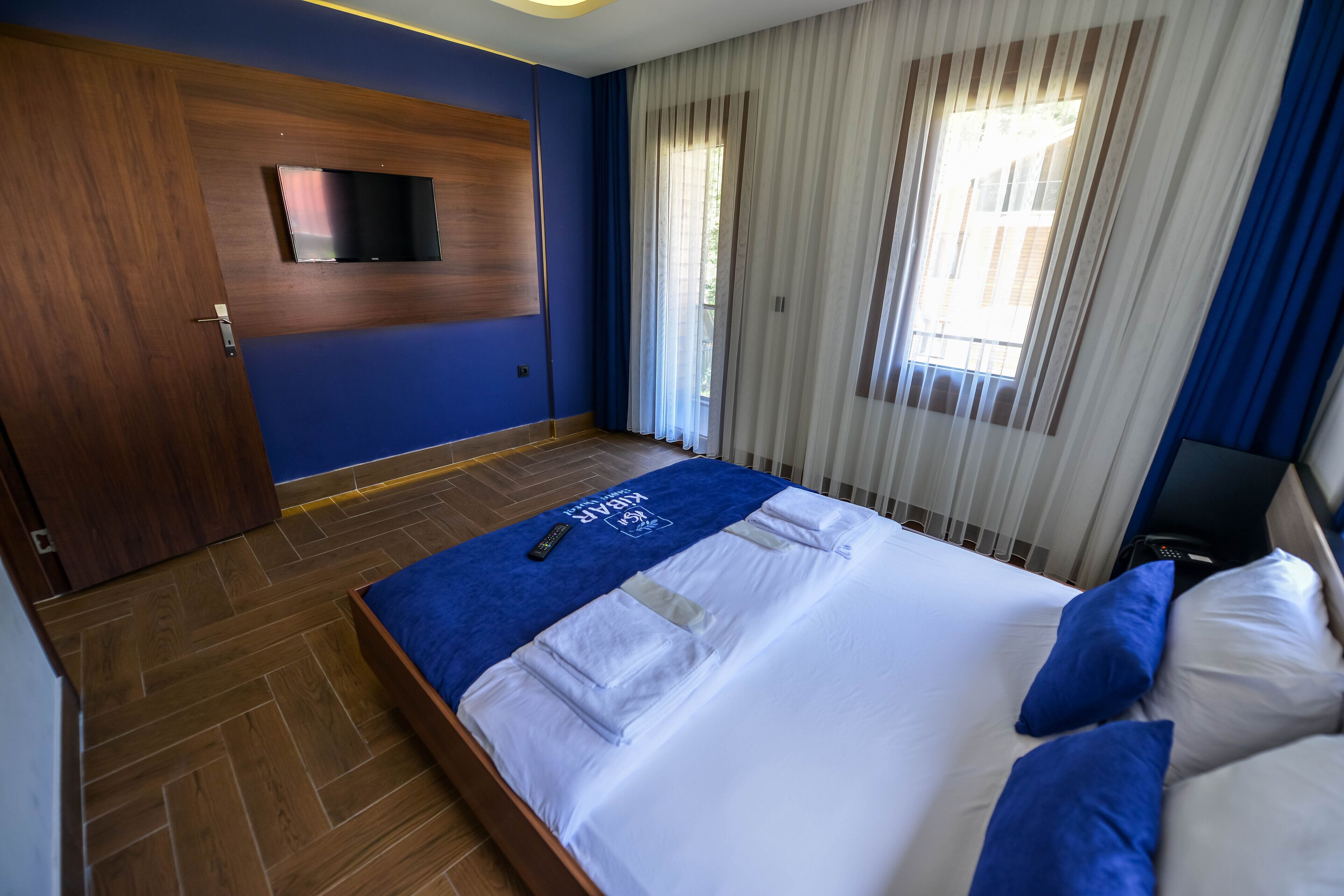 A hotel room with a bed, a TV mounted on the wall, and a window with curtains.