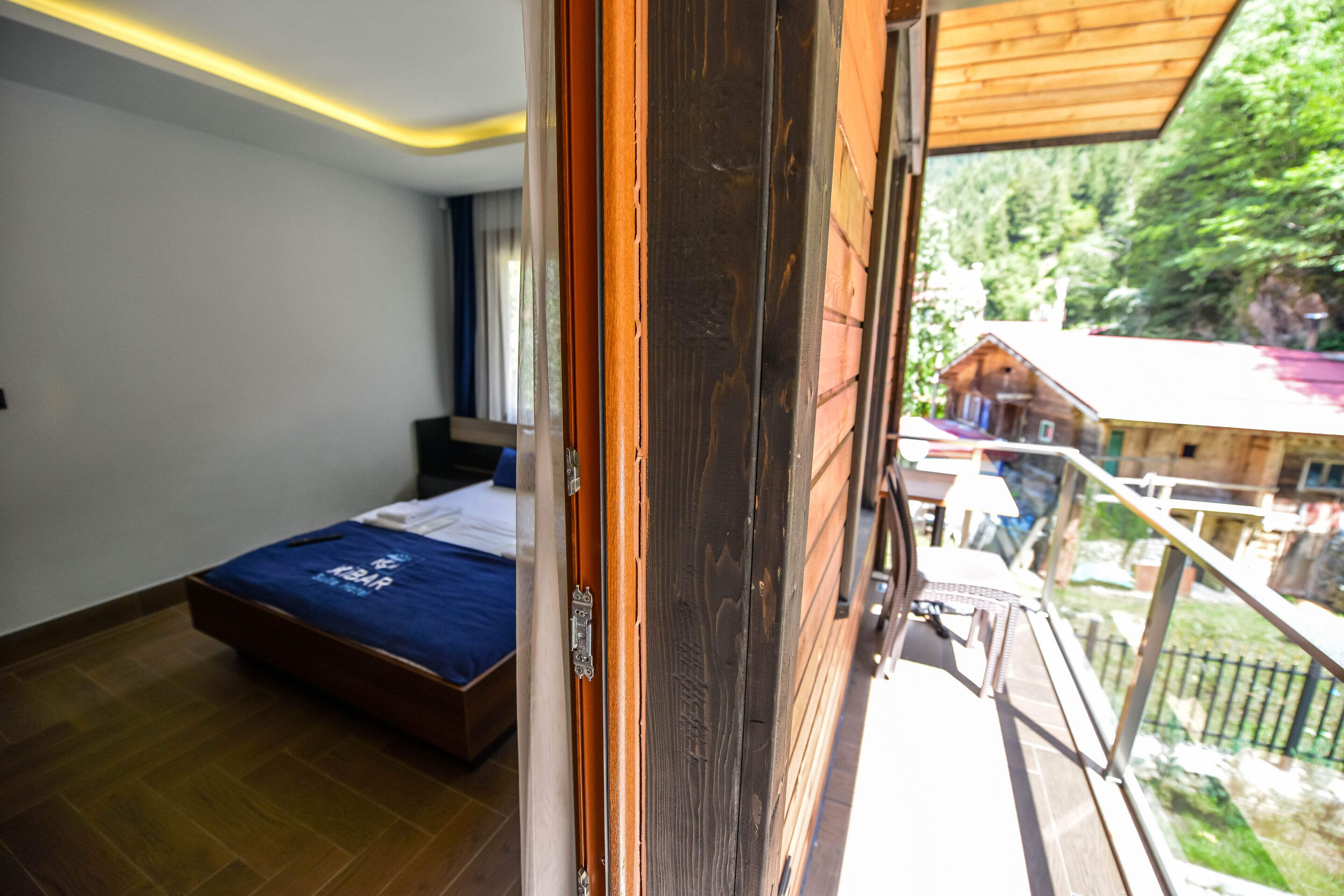 Ein Schlafzimmer mit einem Bett, einer Holztür und einem Balkon mit Blick auf ein Haus und Bäume.