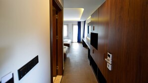 Un pasillo de hotel con una puerta de madera, una cama y un televisor montado en la pared.