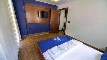 A hotel room with a wooden floor, a bed with a blue bedspread, and a TV mounted on the wall.