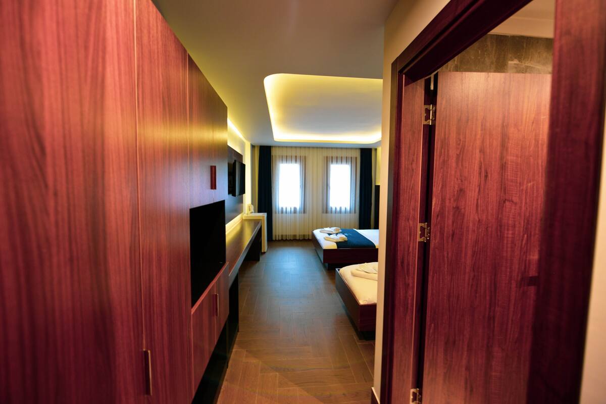A hotel room with a wooden wardrobe, a bed, a bedside table, and a TV.