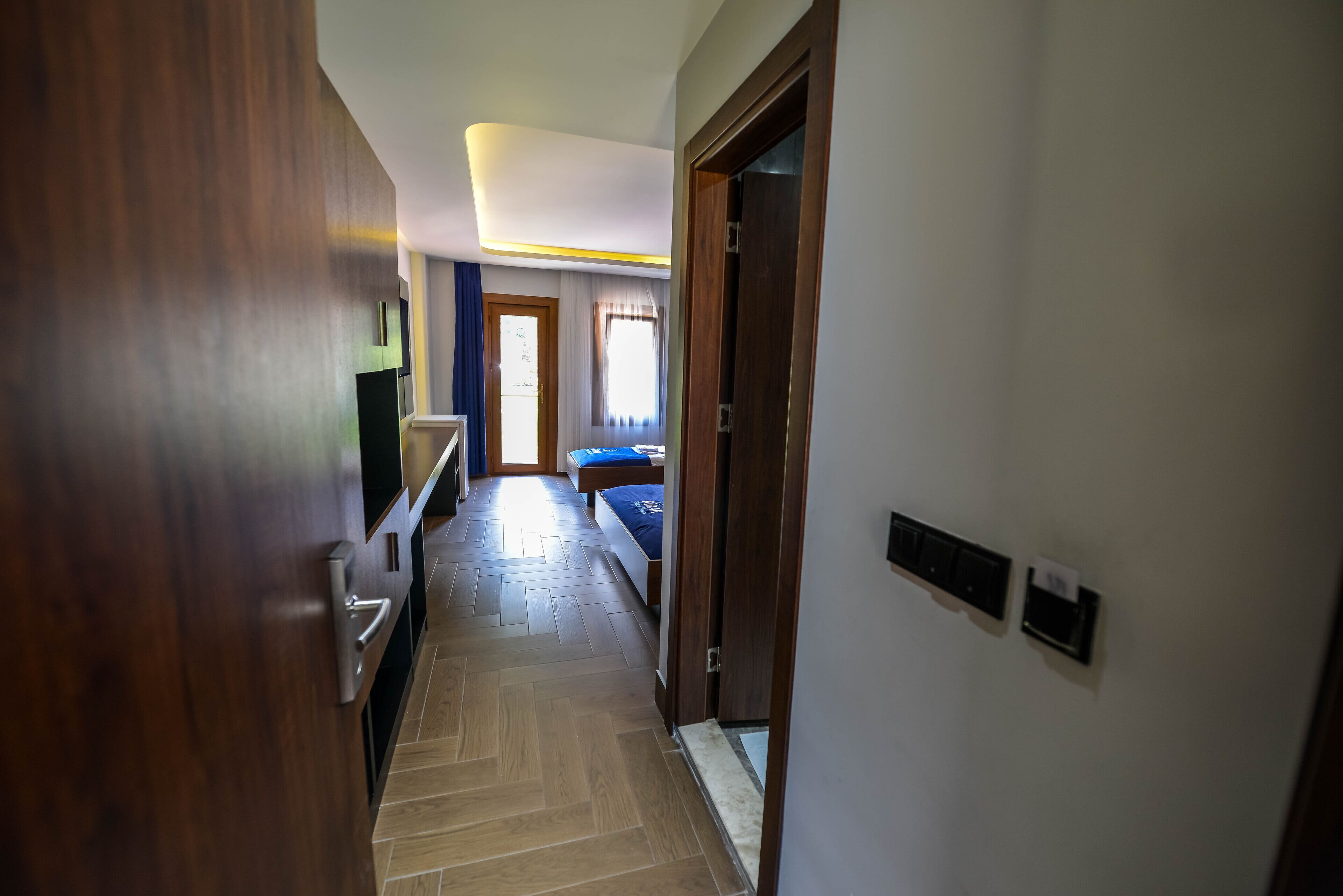 A hallway leading to a bedroom with a bed, a door, and a wall-mounted thermostat.