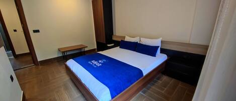 A neatly made bed with a blue blanket, a wooden headboard, and a bench beside the bed.