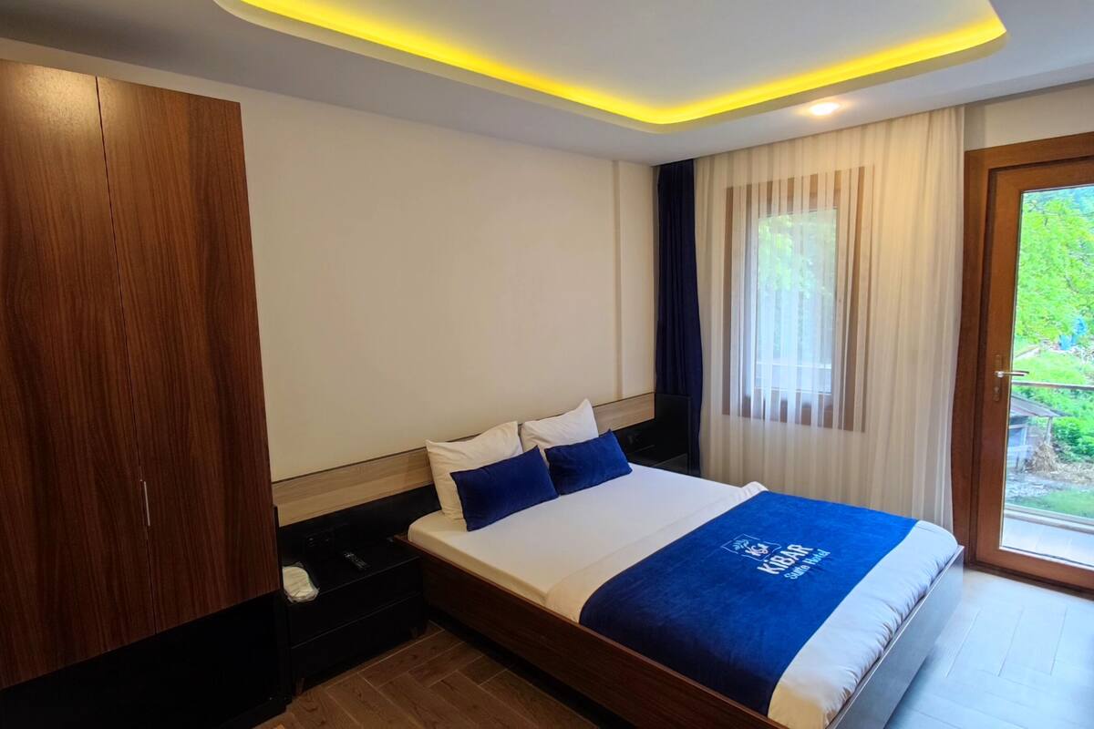 A hotel room with a bed, wooden wardrobe, and a view of greenery through the window.