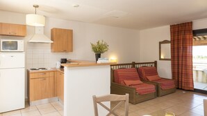 A compact kitchen with wooden cabinets, a microwave, and a small dining area with a table set for two. - Odalys Residence Les Hameaux de Capra Scorsa (Belgodere)