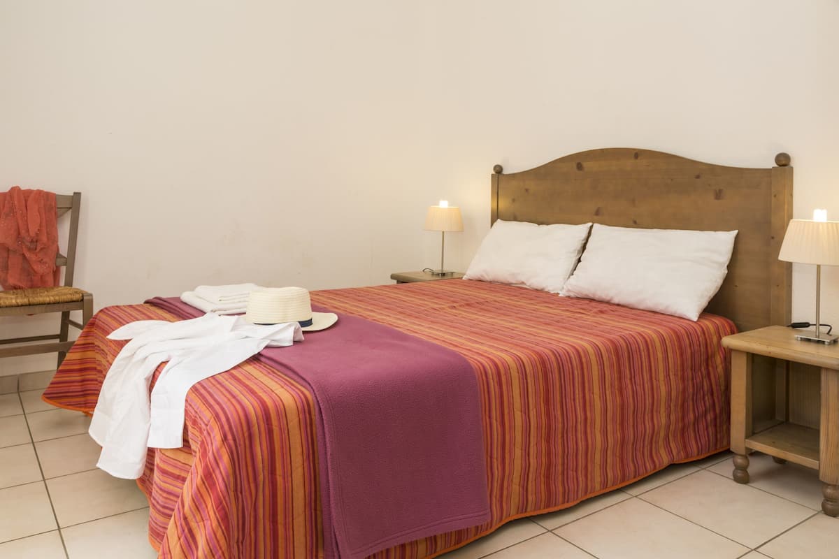 A neatly made bed with striped bedding, two bedside lamps, and a chair with a towel and hat.