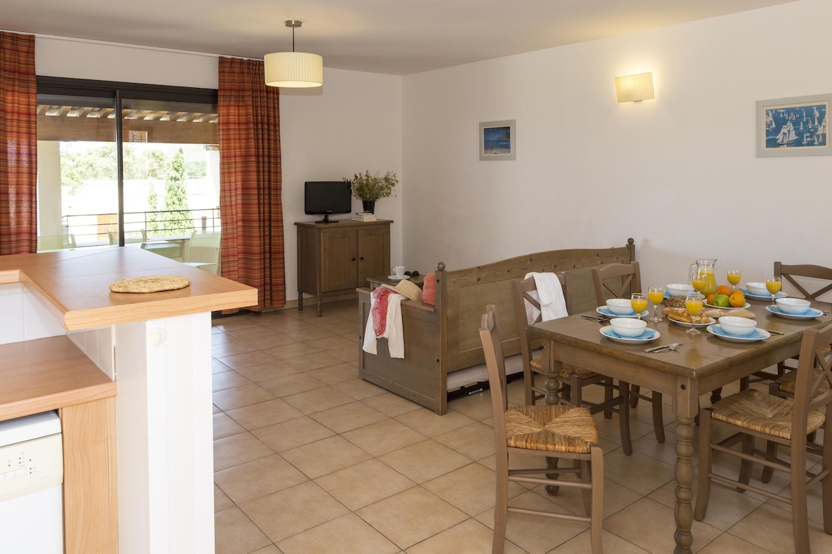 Un comedor con una mesa de madera dispuesta para el desayuno, un sofá y un televisor sobre un mueble.