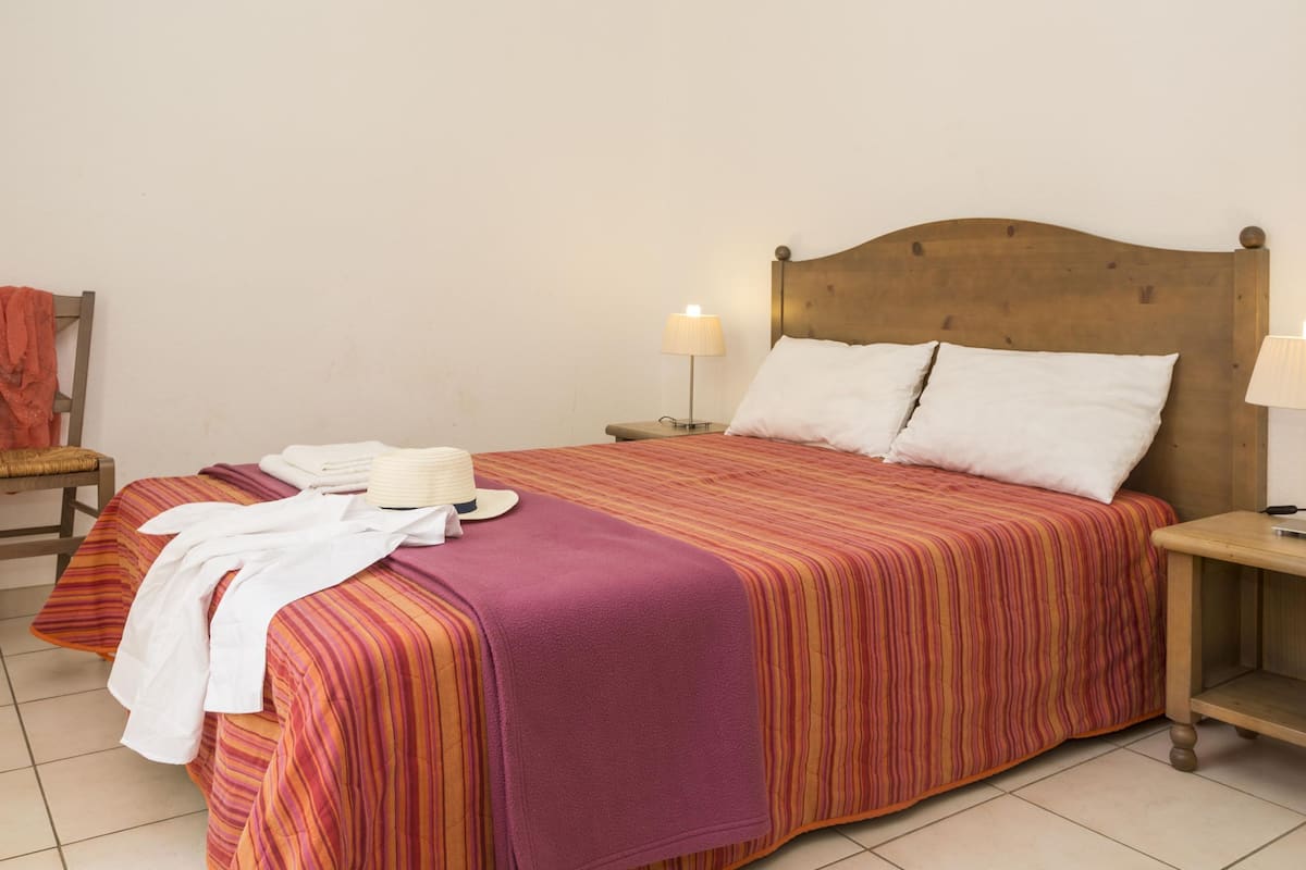 A bed with a striped bedspread, two bedside lamps, a wooden headboard, and a chair with a towel.