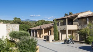 A residential area with a two-story building, a parked motorcycle, and a clear view of the mountains in the background. - Odalys Residence Les Hameaux de Capra Scorsa (Belgodere)