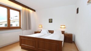 A bedroom with a wooden bed, two bedside tables, a window with curtains, and two wall-mounted lamps.