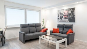 A modern living room with two grey sofas, a glass coffee table, and a large black-and-white cityscape painting on the wall. - Business Apartments Ratingen West (Ratingen)