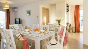 A dining area with a glass table, white chairs, and a television on a cabinet. - Résidence Odalys Casa d'Orinaju (Oletta)