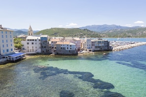 Un poble costaner amb edificis al passeig marítim, aigua cristal·lina i muntanyes al fons.
