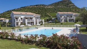 A hotel with a swimming pool surrounded by sun loungers and a mountain backdrop. - Résidence Odalys Casa d'Orinaju (Oletta)