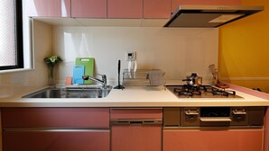 A kitchen with pink cabinets, a stainless steel sink, a gas stove, and a dish rack.