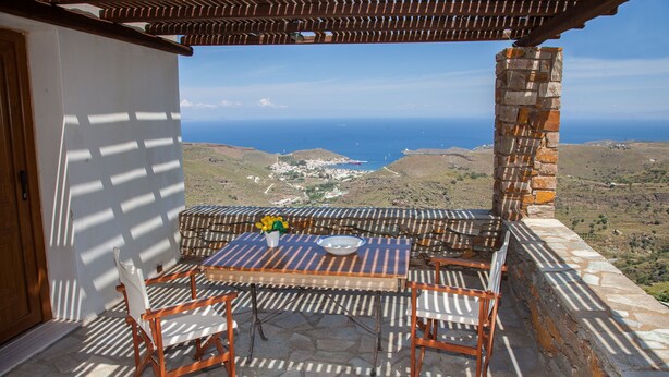 A terrace with a table and chairs, overlooking a coastal landscape. - Villa Karthea III (Kea)