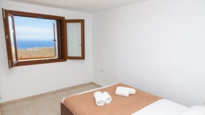 A bedroom with a large window, a bed with a brown bedspread, and two rolled towels on the bed. - Villa Karthea III (Kea)
