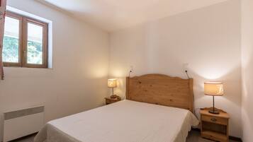 Une chambre avec un lit simple, deux tables de chevet avec des lampes, une fenêtre avec des rideaux et un radiateur.
