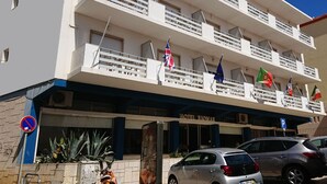 A hotel with a modern design, featuring multiple balconies with railings, flags, and a clear blue sky. - Hotel Riomar (Lagos)