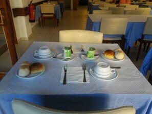 Una mesa de comedor con panes, una taza de té, un recipiente verde y una tetera.