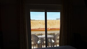 A room with a bed, a window with curtains, and a view of a balcony with chairs and a table. - Hotel Riomar (Lagos)