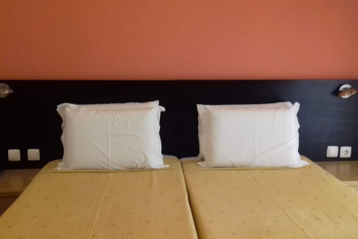 A double bed with two white pillows and a dark headboard in a room with orange walls.