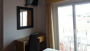 A hotel room with a desk, chair, TV, and a large window with a view of the outside. - Hotel Riomar (Lagos)