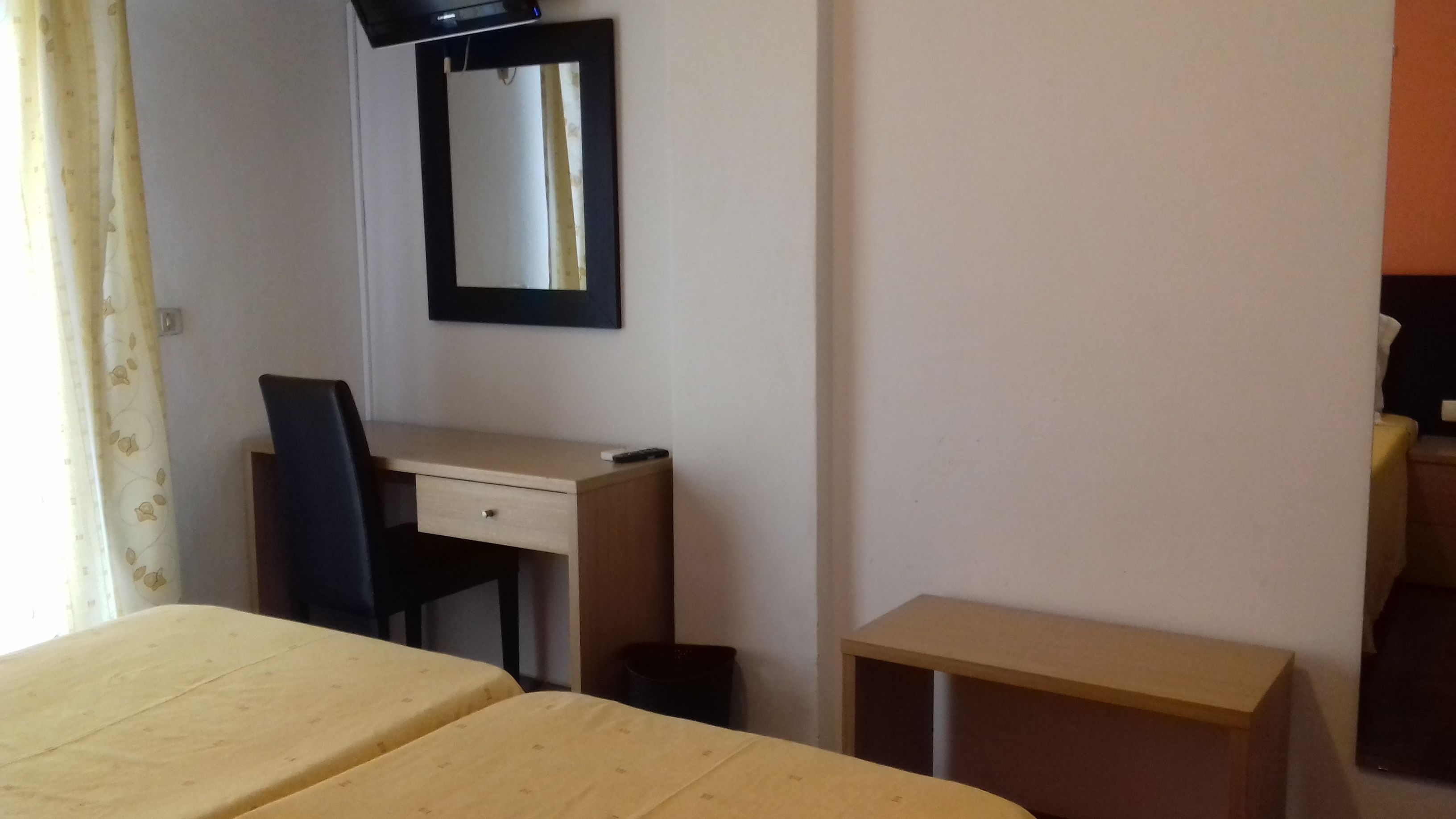 A room with a bed, a desk, a chair, a small table, and a mirror on the wall.