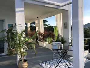 Un espace extérieur abrité, doté de piliers blancs, de plantes en pot et d’une table avec des chaises.