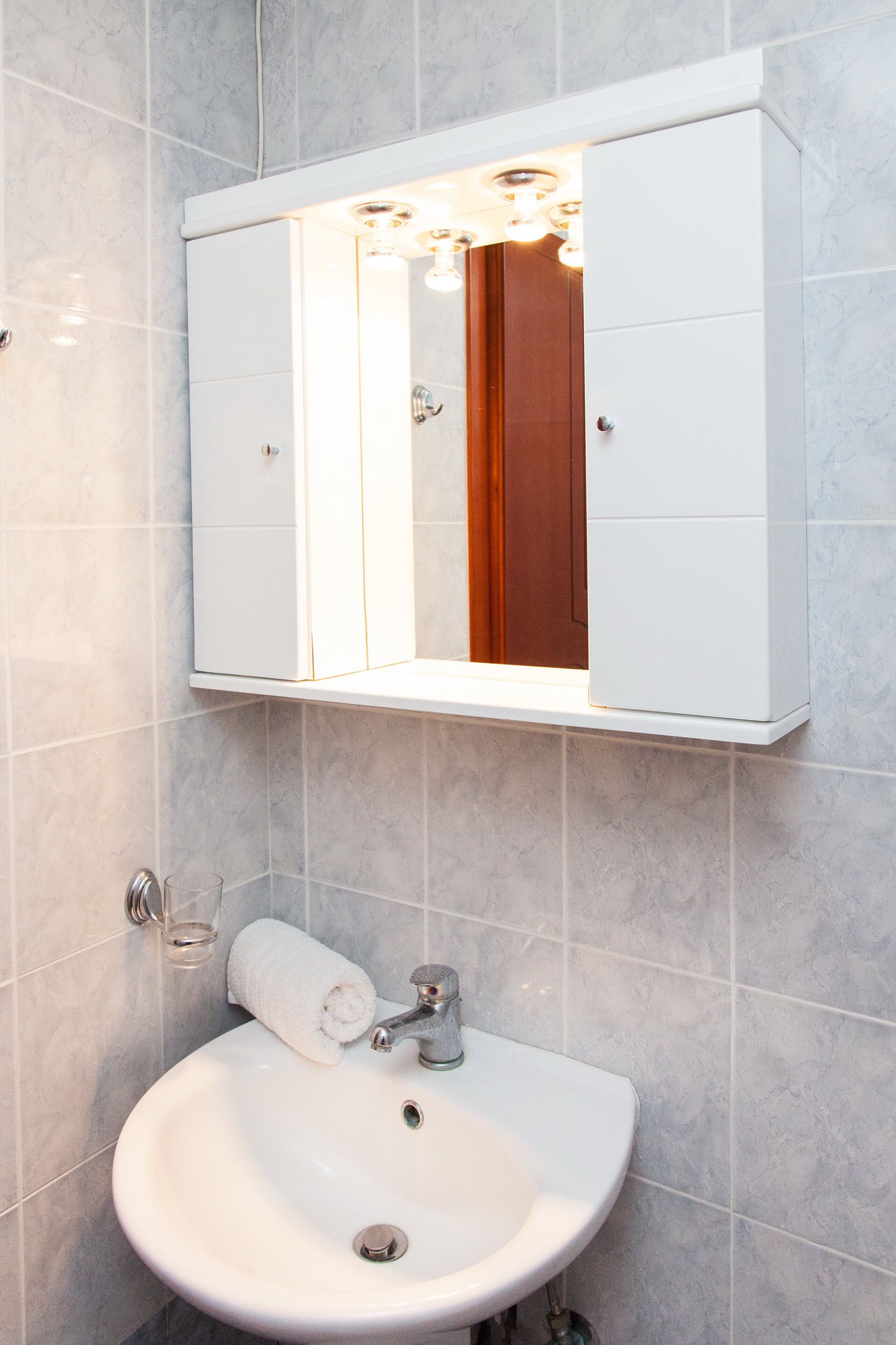 Un baño con un lavabo blanco, un espejo encima y una puerta de madera.