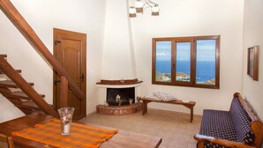 Ein gemütliches Wohnzimmer mit einer Holztreppe, einem Kamin, einer Couch und einem Esstisch.