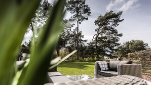 A wicker outdoor seating area with a view of a grassy yard and trees. - Kamphof Usedom Ferienanlage (Loddin)
