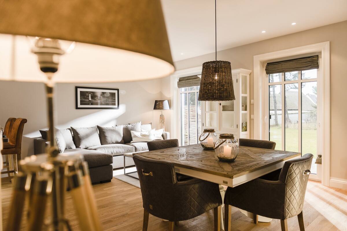 Un comedor con una mesa y sillas de madera, una lámpara colgante y vistas al exterior a través de un ventanal.
