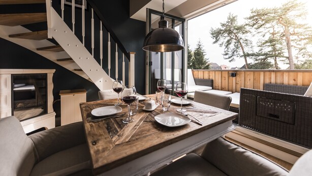 A dining area with a wooden table set for two, a staircase, and a view of trees outside. - Kamphof Usedom Ferienanlage (Loddin)