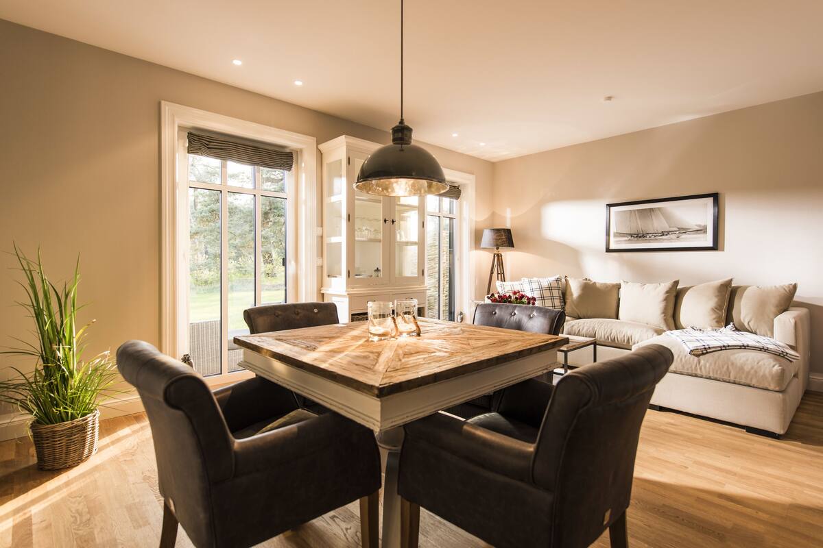 Un comedor con una mesa y sillas de madera, una lámpara colgante, un sofá y un cuadro en la pared.