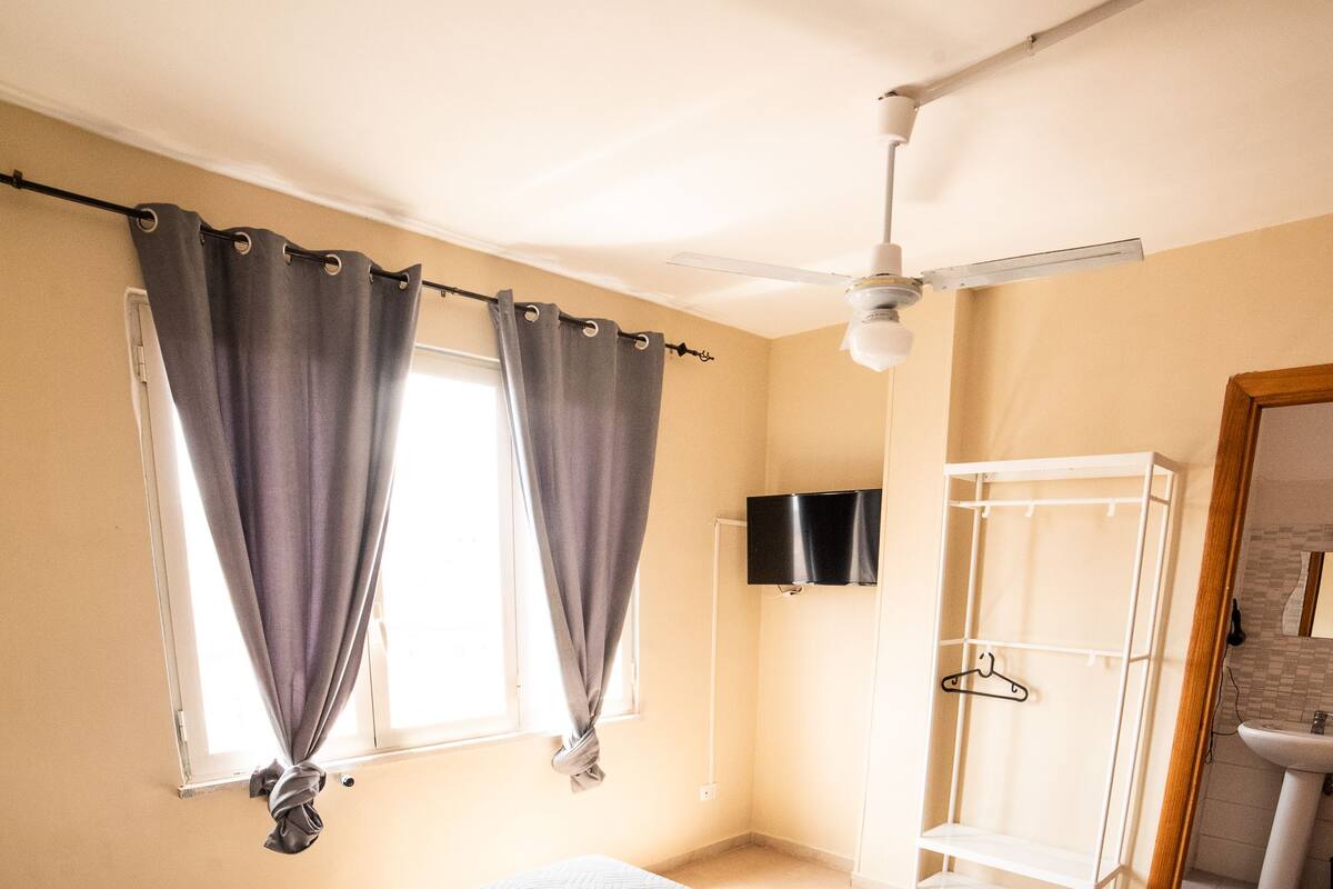 A hotel room with a bed, a shower area, and a TV mounted on the wall.